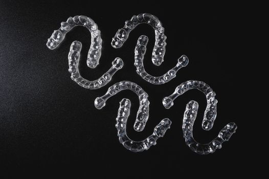 a pattern of invisible plastic aligners lie on a black background