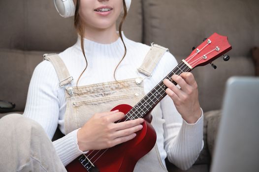 close-up, a woman or girl plays the ukulele while sitting at home, on the floor. distance learning