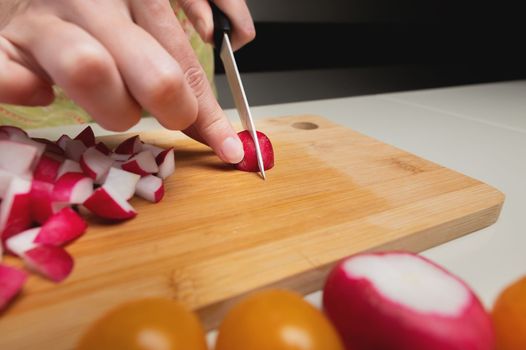 female hands hold a radish on a board, close-up. layout or banner for culinary website