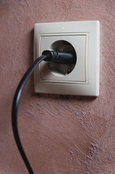 White electrical outlet on the wall with a black wire inserted. close-up, home decor