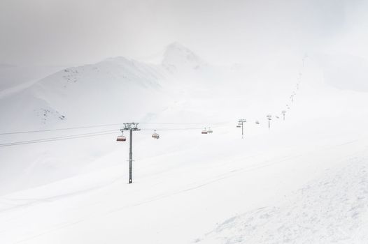Cable car climbs high mountain in snowy weather, ski resort in winter