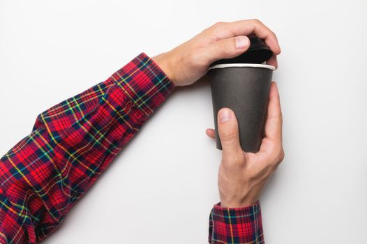 Hands in a shirt open the lid from a black paper cup on a white background
