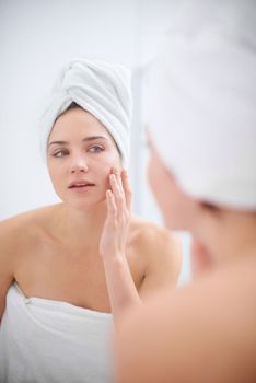 Personal beauty regime. A woman looking in her bathroom mirror with a towel on her head