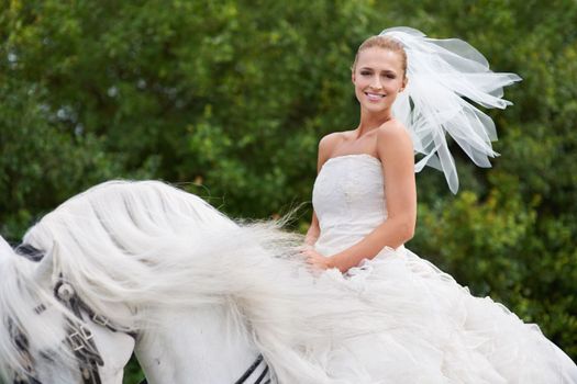 Riding to meet her white knight on the special day. A gorgeous young bride riding a white horse on her wedding day.