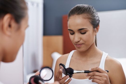 Shes got a weakness for cosmetics. An attractive young woman applying makeup in the mirror.