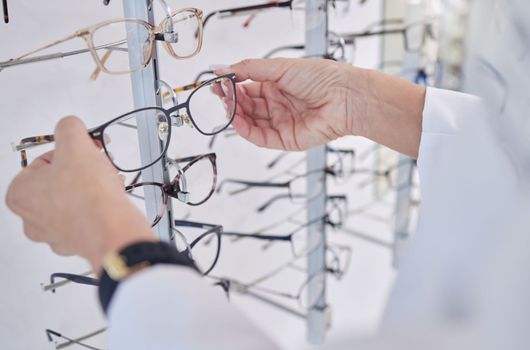 Working, decision and hands of an optometrist with glasses, eyewear and frame for vision in a shop. Healthcare, retail and optician with a choice of eyeglasses for visual service and optics in store