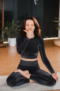 A woman in a black tracksuit sits on a yoga mat in a lotus position in the gym