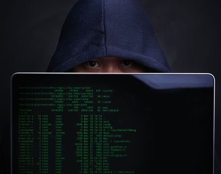 Someones been keeping a watch of your every move online. Portrait of a hacker holding up a laptop against a dark background.
