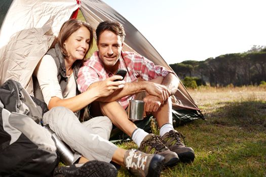 Enjoying a camping adventure. A young couple checking hiking trials on a cellphone.