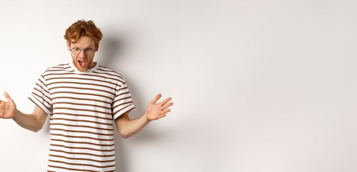 Impressed redhead man in glasses showing length of something big, demonstrate large size and looking amazed, standing over white background