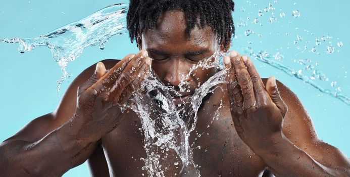 Water, splash and cleaning face for hygiene with a model black man in studio on a blue background for hydration. Bathroom, skincare or wellness with a male washing himself for natural skin treatment