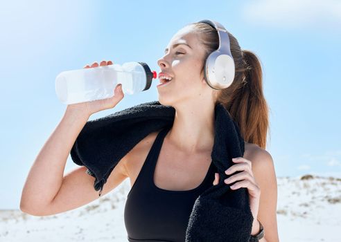 Beach, workout and drinking water with headphones music for exercise, fitness and training break. Wellness, relax and sport woman streaming audio and resting body after cardio with water hydration.