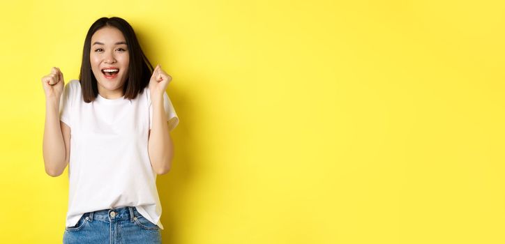 Carefree asian girl dancing and having fun, posing in white t-shirt against yellow background