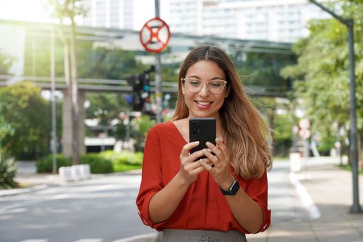 Beautiful smart woman with glasses using mobile phone walking in Sao Paulo modern sustainable metropolis in Brazil