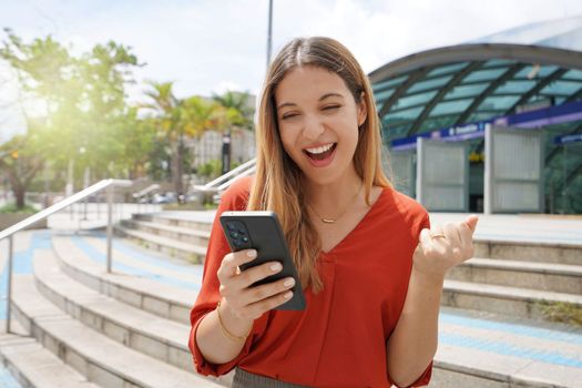 Excited casual woman celebrating good news on her smartphone in Brooklin district of Sao Paulo, Brazil