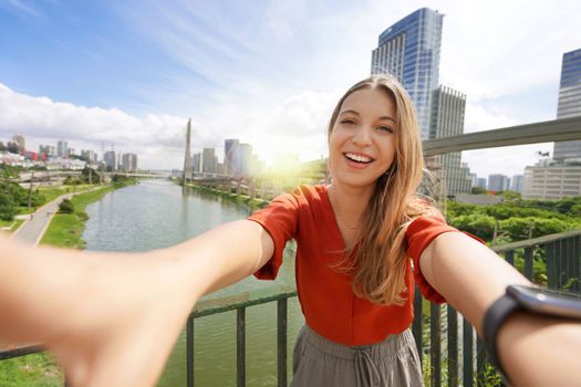 Happy smiling girl takes self portrait with Ponte Estaiada bridge and cityscape of Sao Paulo metropolis, Brazil