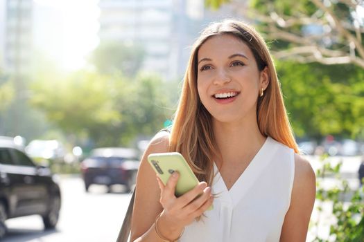 Brazilian confident businesswoman looking away holding smartphone outdoors on summer 