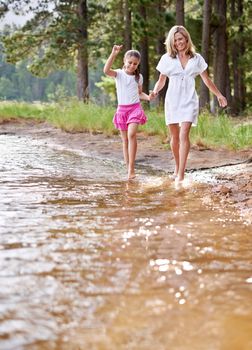 Taking a stroll with mom. A cute little girl running through a wilderness stream with her mother.