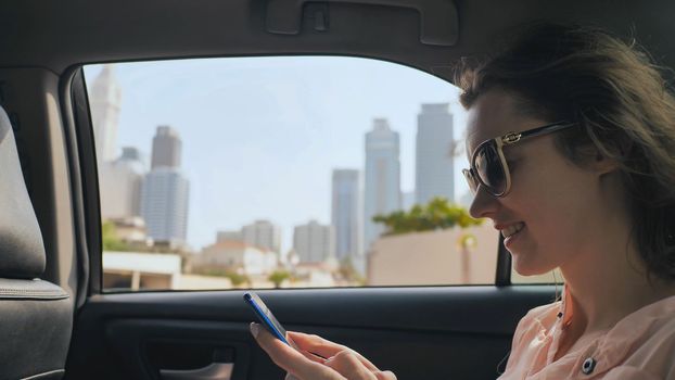 A girl in a moving car is typing a message on the phone. Dubai city.