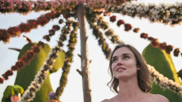 Girl on the background of hanging daisies of fresh flowers in a city park.