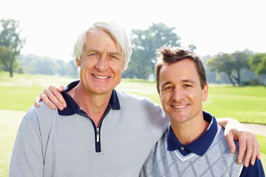Father and son on the golf course. Closeup of father and son standing on golf course with arms around and smiling.