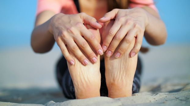 Beautiful blond woman doing stretching exercises on the beach. Close-up of foot