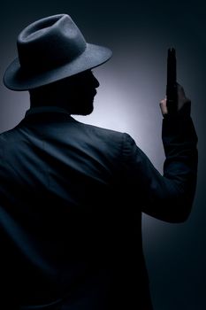 Gangster, silhouette or holding gun on studio background in secret spy, isolated mafia leadership or crime security. Model, man or dark hitman and weapon suit, fashion clothes or bodyguard aesthetic