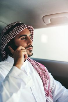 Ambition drives him. a young muslim businessman using his phone while traveling in a car.