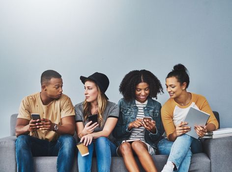 Living their lives online. Studio shot of young people sitting on a sofa and using wireless technology against a gray background