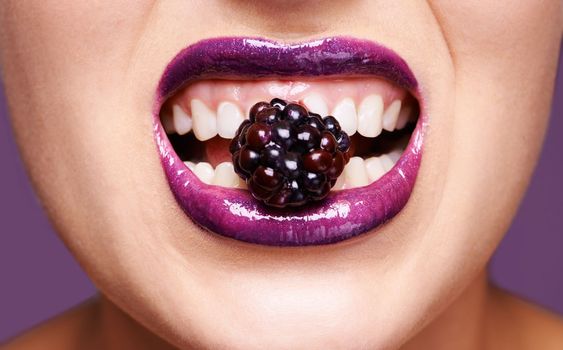 Blackberry bites. a woman wearing purple lipstick and biting into a blackberry.