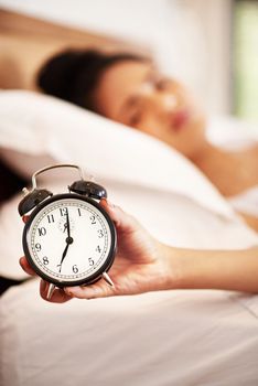 Get a bright and early start to your day. Portrait of a young woman holding an alarm clock while waking up from bed in the morning.