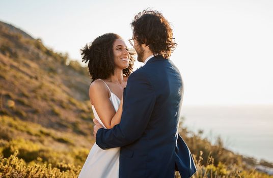 Marriage, love and bride with groom on mountain for wedding ceremony, commitment and celebration. Romance, happiness and interracial couple bonding, hug and smile with ocean, nature and outdoors