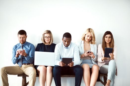 They live for technology. a group of work colleagues seated next to each other while using electronic devices against a white background.