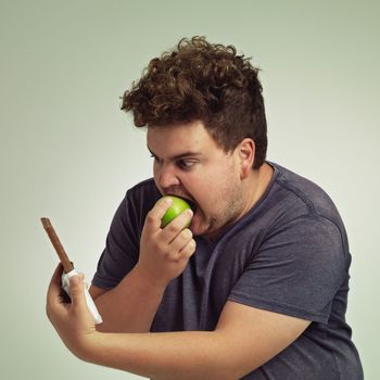 Dodge temptation - stick to your diet. an overweight man taking a bite of an apple while looking at a chocolate.