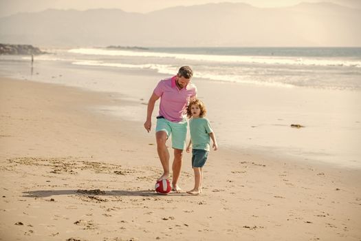 cheerful kid and dad running on beach in summer vacation with ball, friendship