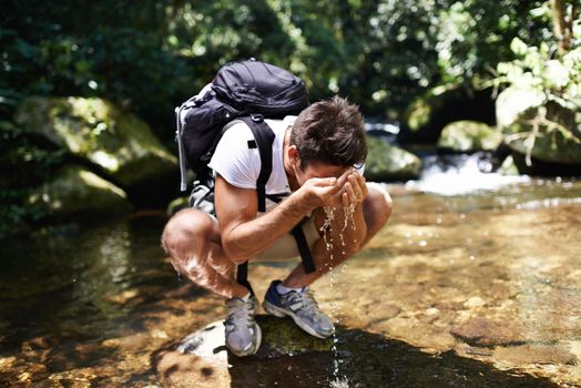 Stopping for a refreshing break. a young man splashing cool water on his face while hiking near a stream.