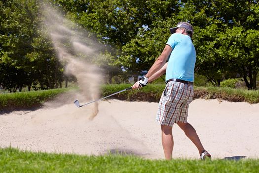 Playing his way out of a ditch. A mature man playing a golf shot from a sand bunker.