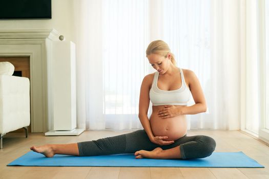 Her body may be changing but her lifestyle choices havent. a pregnant woman doing yoga on an exercise mat at home.