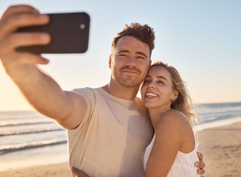 Phone, selfie and happy couple on the beach on vacation for their romantic honeymoon celebration. Happiness, love and young man and woman taking picture together by the ocean or sea while on holiday.