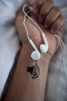 Music makes me escape. earphones in an unrecognizable personss closed hands and a tattoo of a speaker on his wrist.