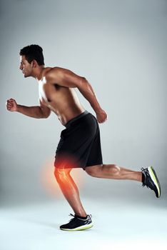 One wrong step can end your workout. Studio shot of a sporty young man running with a knee injury against a grey background.