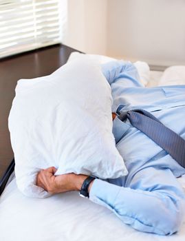 The stresses of business. A businessman covering his face with a pillow