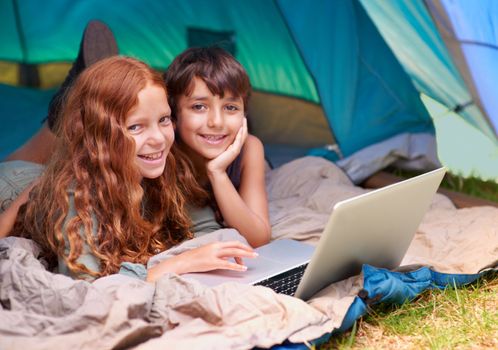 Accessing the web from the wilderness. A young brother and sister surfing the web while out camping.