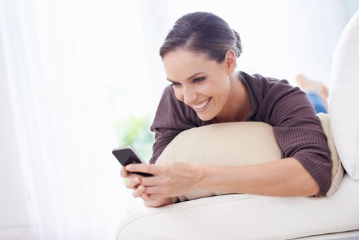 Sending a quick text. A young woman lying on her couch sending a text message.