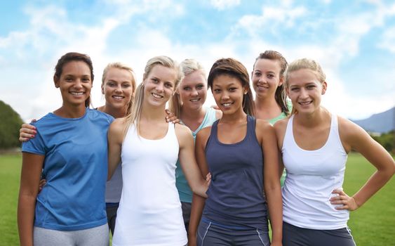 Achieving our fitness goals as a team. A group of young woman in sports clothing smiling at the camera while standing on a sportsfield.