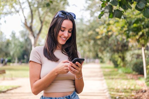 smiling woman typing on mobile phone in a park