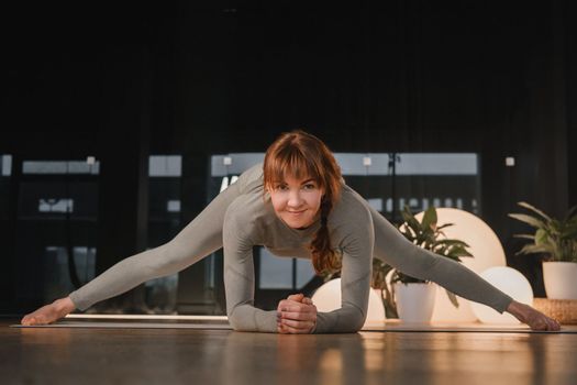 A girl in a gray sports uniform does yoga on a mat in the gym