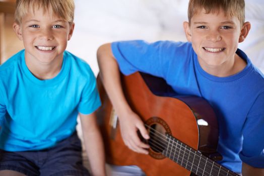 Teaching his brother a few songs...two bothers sitting on a bed with one playing a guitar.