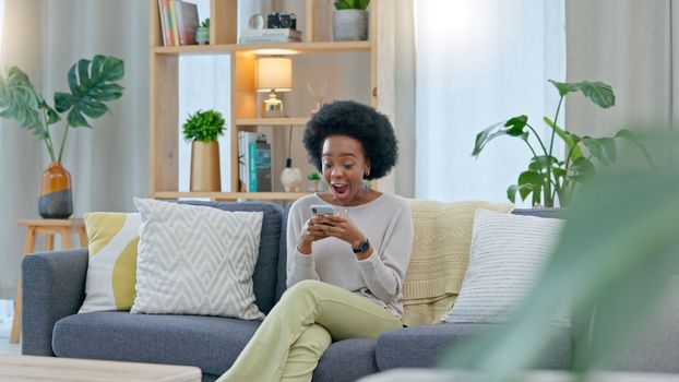 African woman celebrating a new job while sitting at home on a couch. A young females loan is approved via an email on her phone. A happy and excited lady cheering for a promotion on a sofa
