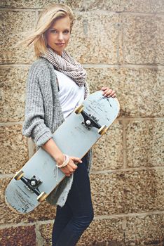 Dont hate me cause you cant out-skate me. Cropped portrait of an attractive young woman carrying her skateboard against a brick wall.